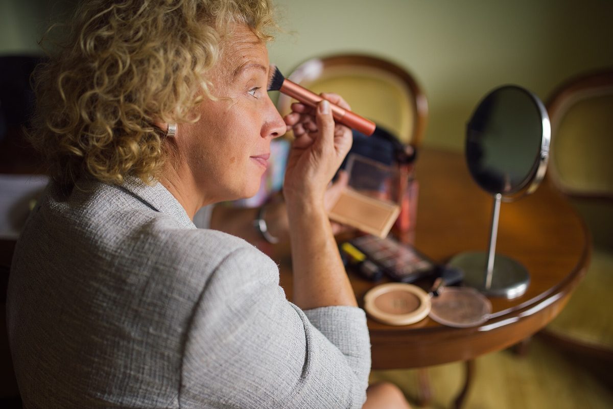 A person applying makeup with a brush at a dressing table with a mirror
