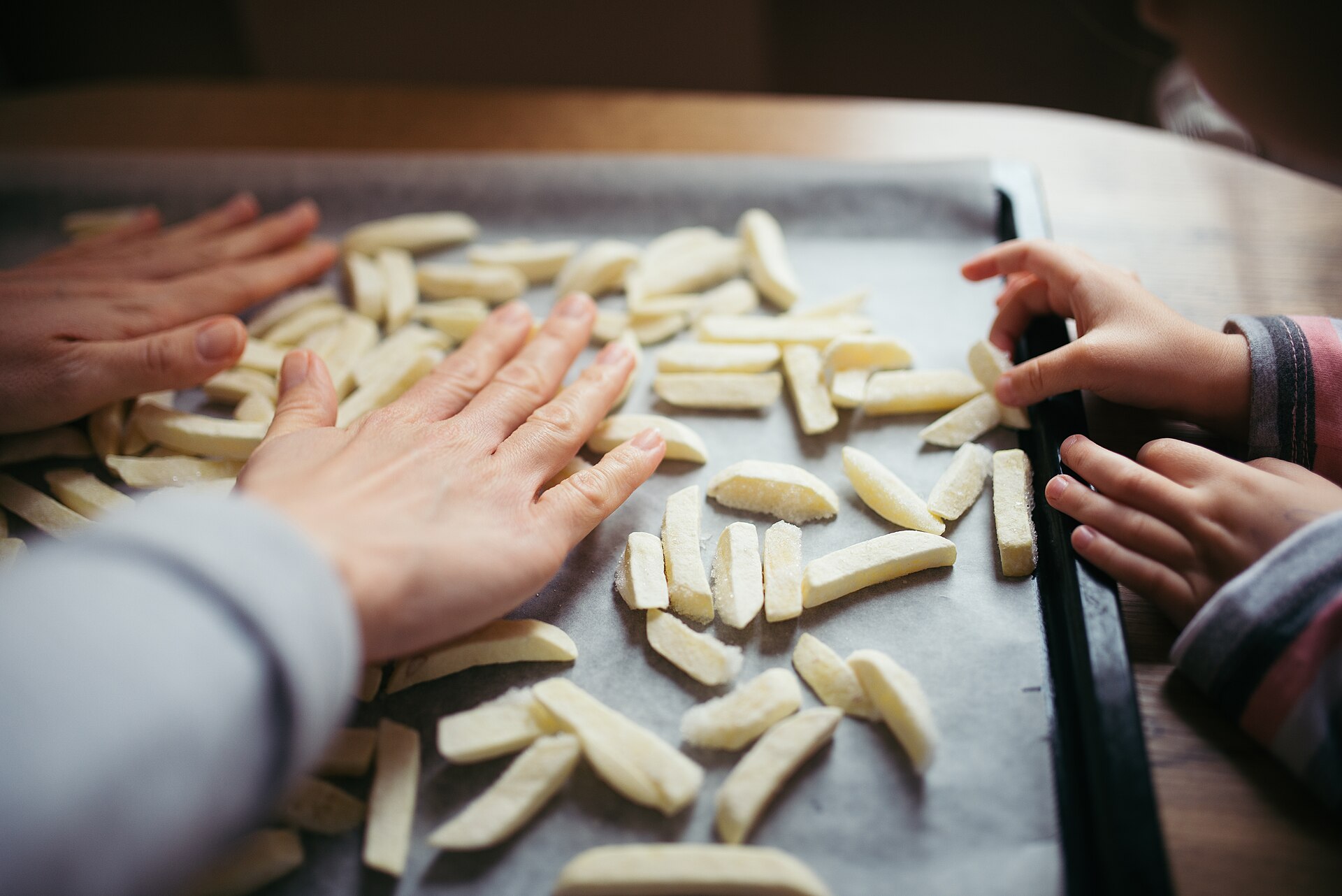A parent and child preparing fresh-cut potato fries together in a kitchen